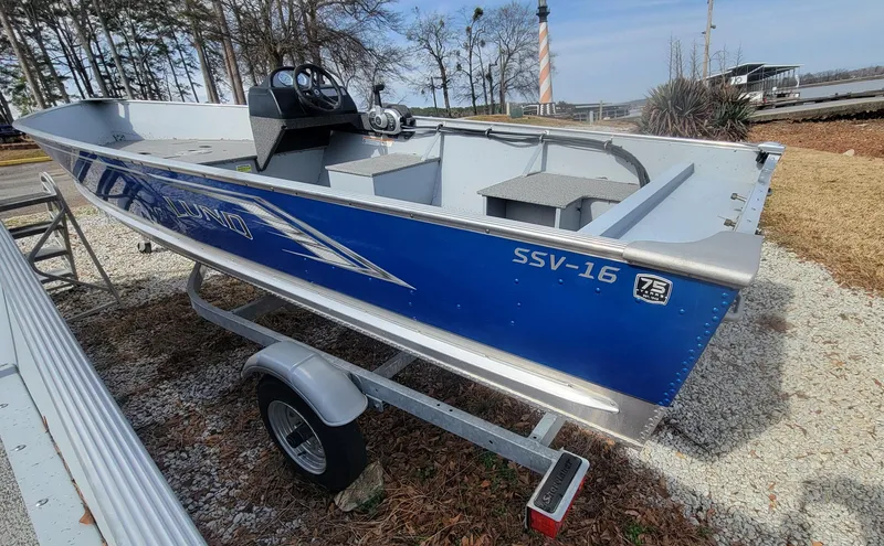 Slide: The Image of 2023 Lund SSV 16 Side Console boat on trailer, blue exterior, parked outdoors. - 4