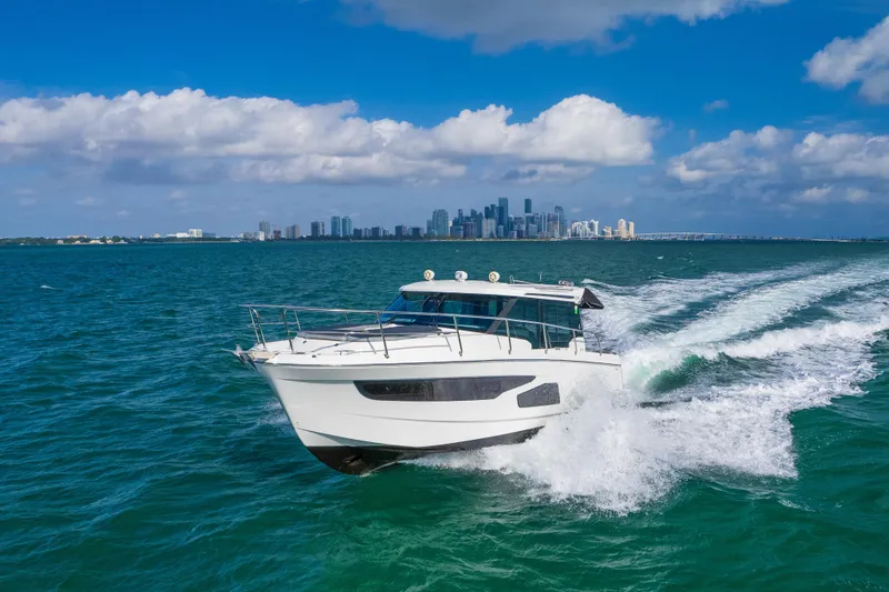 Slide: The Image of 2019 Jeanneau NC 1095 cruising on blue ocean with city skyline in background. - 30