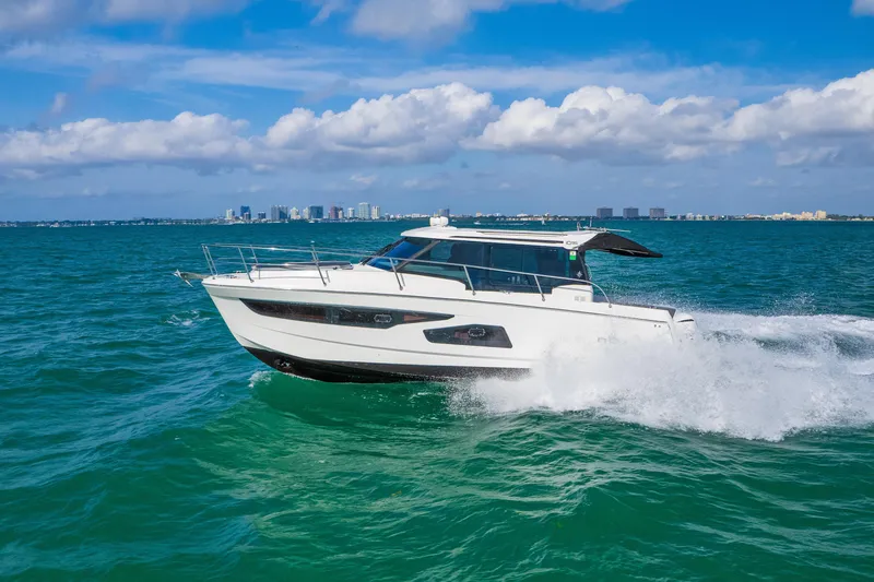 Slide: The Image of 2019 Jeanneau NC 1095 cruising on turquoise ocean with city skyline in background. - 31