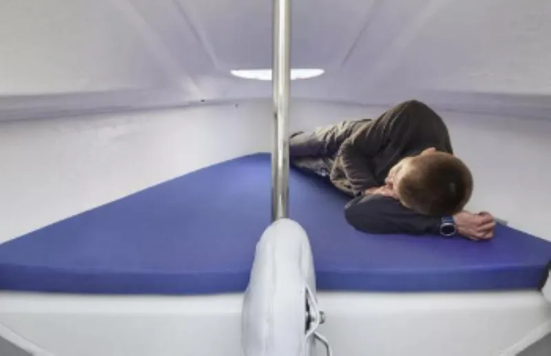 Slide: The Image of Interior cabin of 2025 Beneteau First 18 SE sailboat with person resting. - 9