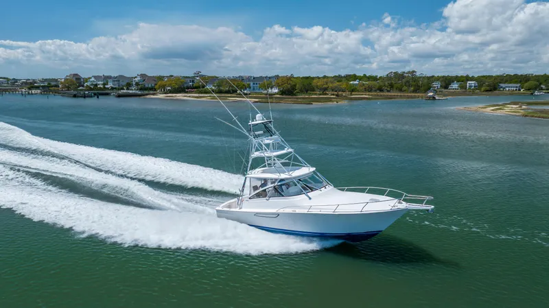 Slide: The Image of A 2013 Viking 42 yacht cruising swiftly on a scenic waterway under a partly cloudy sky. - 8