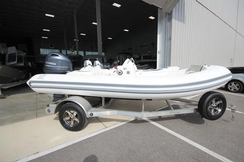 The Image of 2025 Zodiac Yachtline 490 Deluxe NEO 90hp on trailer, parked outside a warehouse. - 2