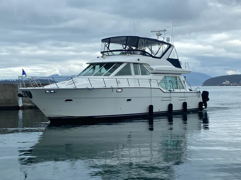 The Image of 2002 Bayliner 5288 Pilothouse yacht docked on calm water under cloudy skies. - 0