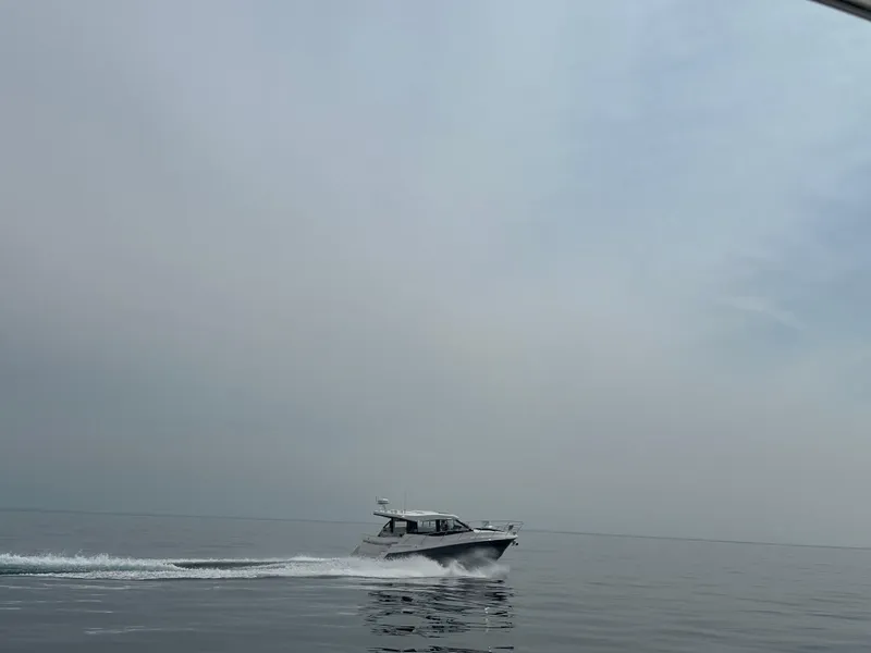 Slide: The Image of 2025 Regal 38 Grande Coupe cruising on calm waters under a cloudy sky. - 2