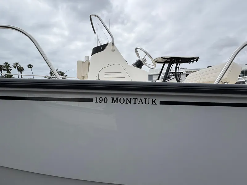 Slide: The Image of 2025 Boston Whaler 190 Montauk boat, side view with console and railing, under cloudy sky. - 2
