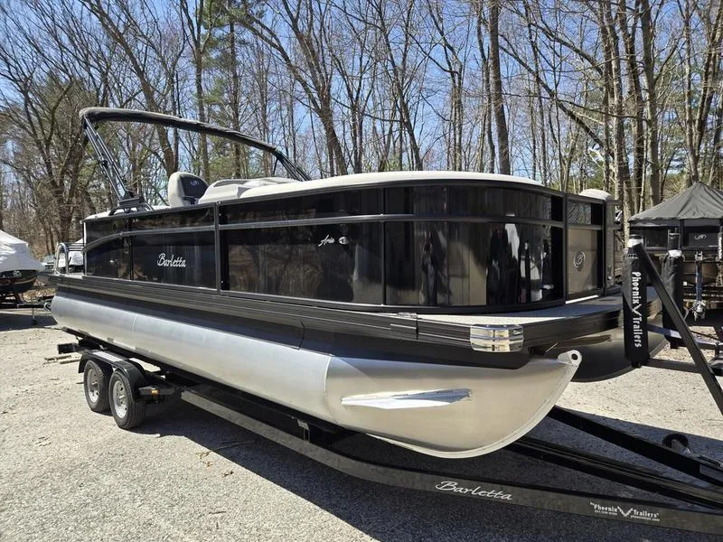 Slide: The Image of 2025 Barletta A22QC pontoon boat on trailer, parked outdoors in wooded area. - 6