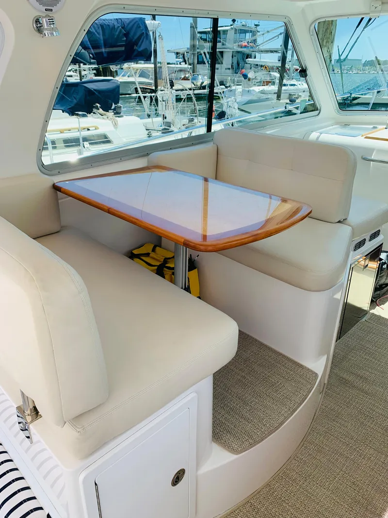 Slide: The Image of 2015 Back Cove 34 Express interior with cushioned seating and wooden table, docked at marina. - 45