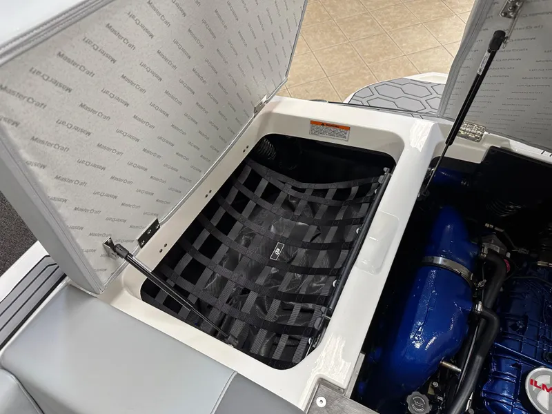 Slide: The Image of 2025 MasterCraft NXT21 boat storage compartment with netting and visible engine components. - 17