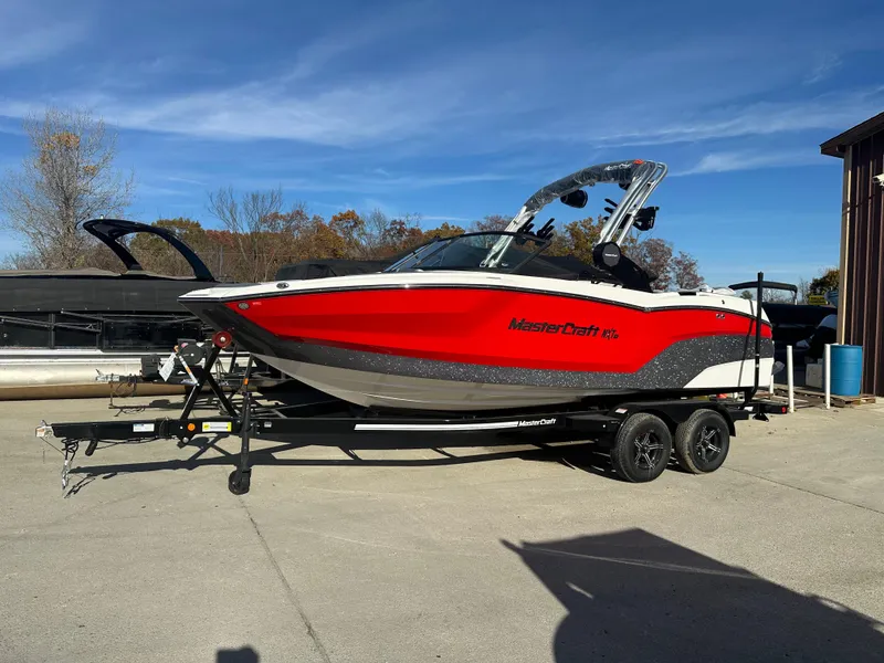 Slide: The Image of 2025 MasterCraft NXT21 boat in red and white on a trailer, parked outdoors. - 2