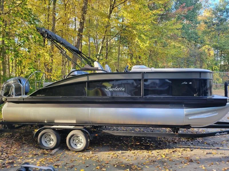 Slide: The Image of 2025 Barletta A20UC pontoon boat on trailer, surrounded by autumn trees. - 1