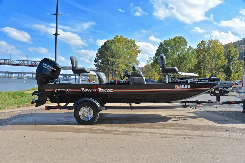 Slide: The Image of 2024 Bass Tracker Classic XL boat on trailer by riverside, under clear blue sky. - 15