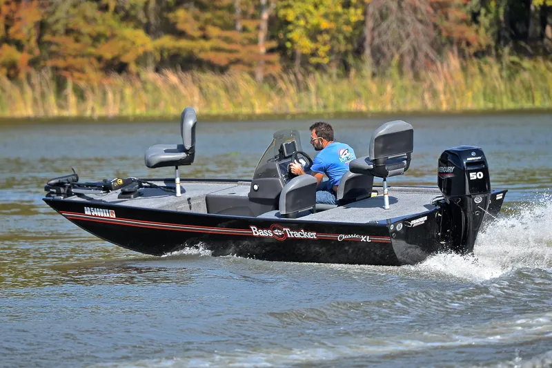 Slide: The Image of 2024 Bass Tracker Classic XL boat cruising on a lake with lush greenery. - 6