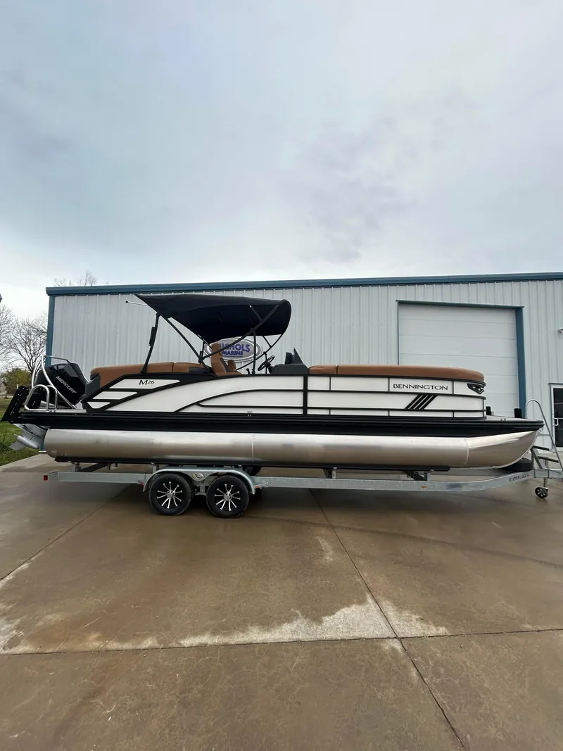 Slide: The Image of 2025 Bennington M26 pontoon boat on trailer, parked outside a warehouse. - 1
