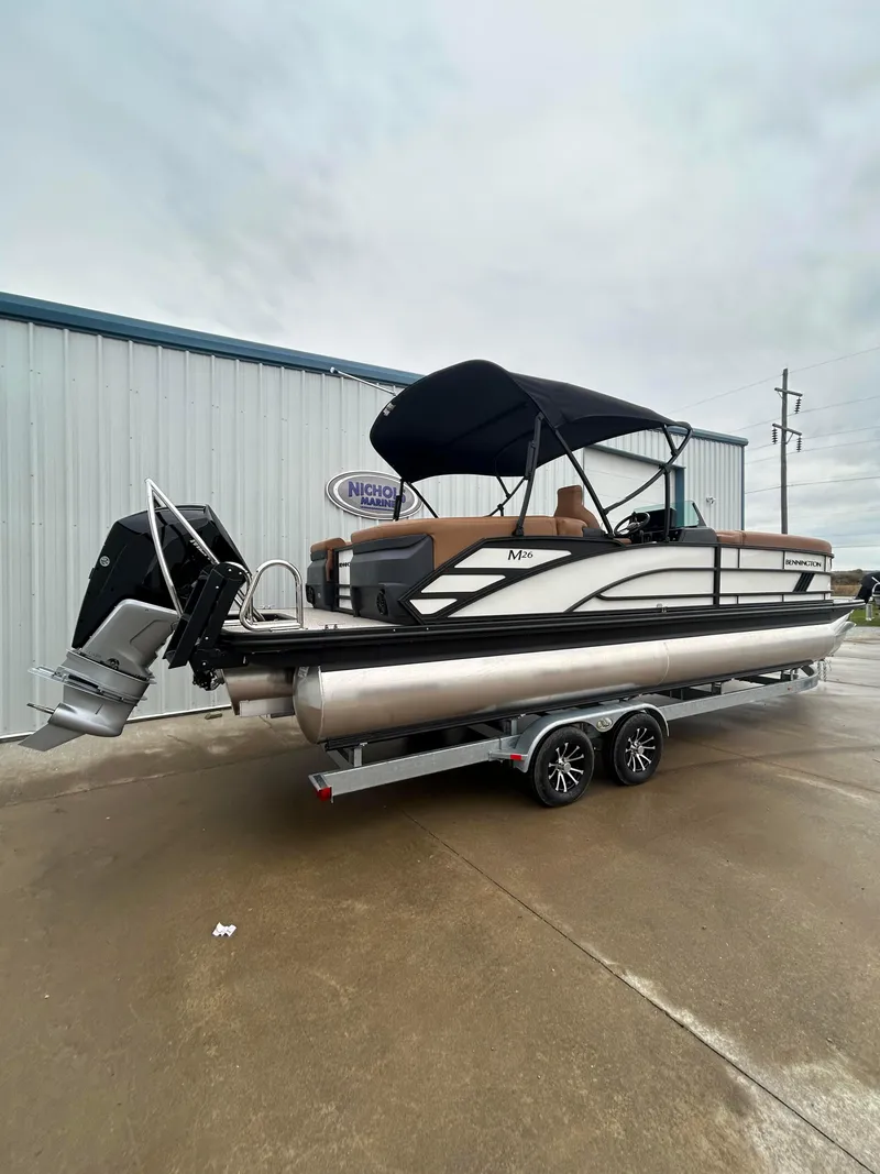 Slide: The Image of 2025 Bennington M26 pontoon boat on trailer, parked outside a building. - 2