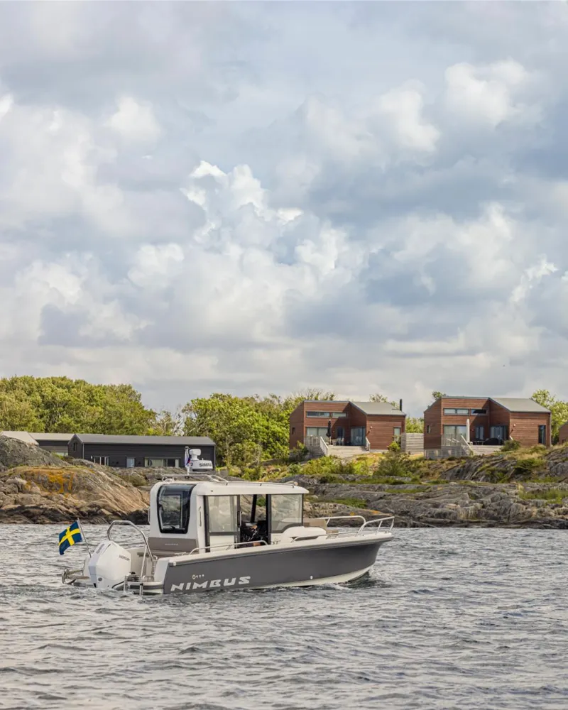 Slide: The Image of Nimbus C8 2025 boat cruising near rocky shoreline with modern houses in the background. - 13