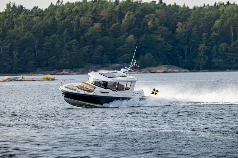 Slide: The Image of Nimbus C9 2025 motorboat cruising on a lake with forested shoreline. - 9