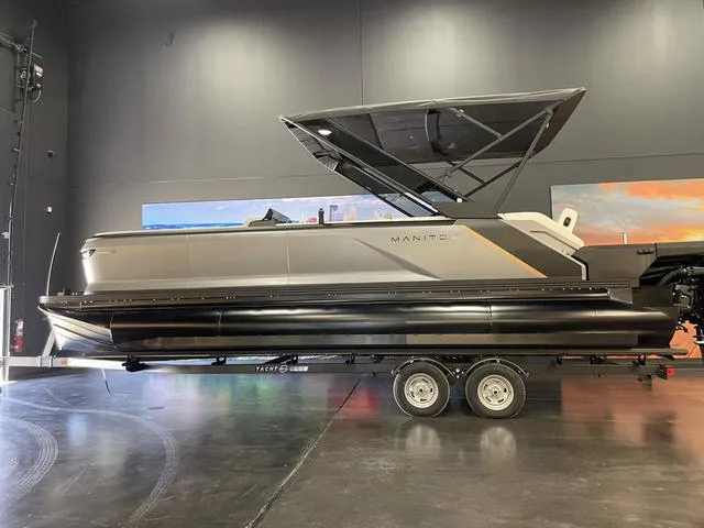 Slide: The Image of 2024 Manitou EXPLORE 24 MAX SGP dual engine boat on trailer in showroom. - 1