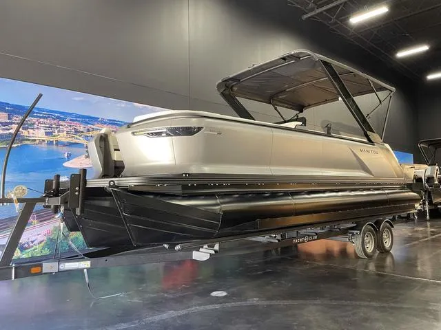 Slide: The Image of 2024 Manitou EXPLORE 24 MAX SGP dual engine boat on trailer in showroom. - 2