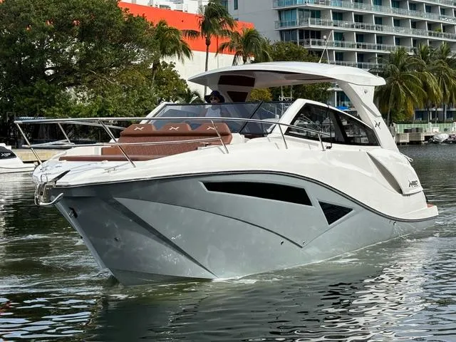 Slide: The Image of 2023 NX Boats 360 cruising on a calm waterway near modern buildings and lush trees. - 0
