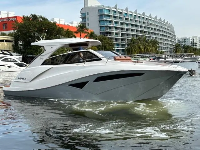 Slide: The Image of 2023 NX Boats 360 cruising in a marina with modern architecture in the background. - 1