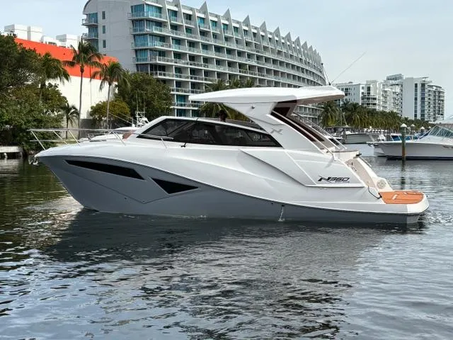 Slide: The Image of 2023 NX Boats 360 yacht on a calm waterfront with modern buildings. - 2