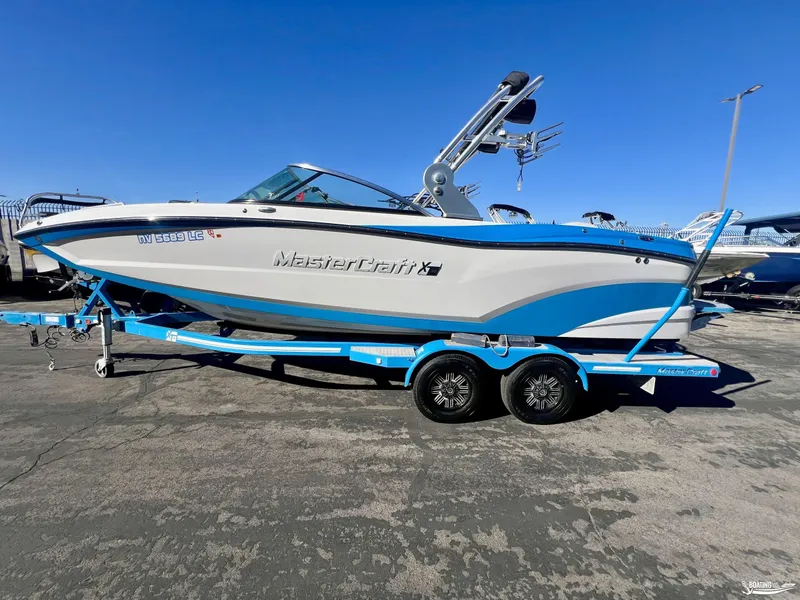 Slide: The Image of 2018 MasterCraft XT22 boat on trailer, blue and white design, parked outdoors. - 2