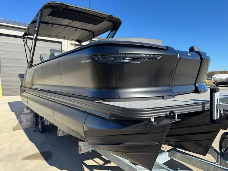 The Image of 2025 Manitou Navigator pontoon boat on trailer, sleek black design, outdoor setting. - 1