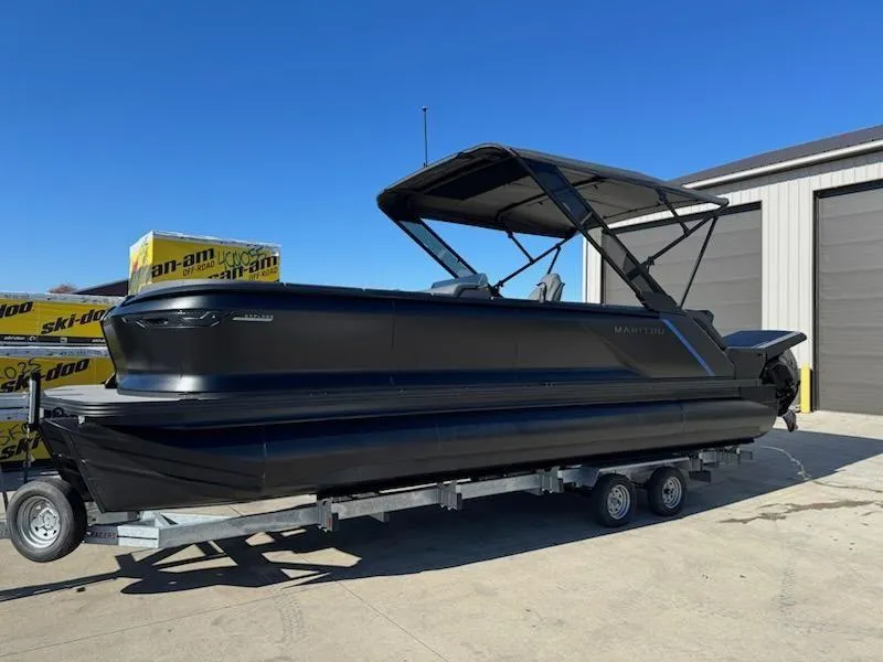 Slide: The Image of 2025 Manitou Navigator pontoon boat on trailer, parked outdoors. - 2