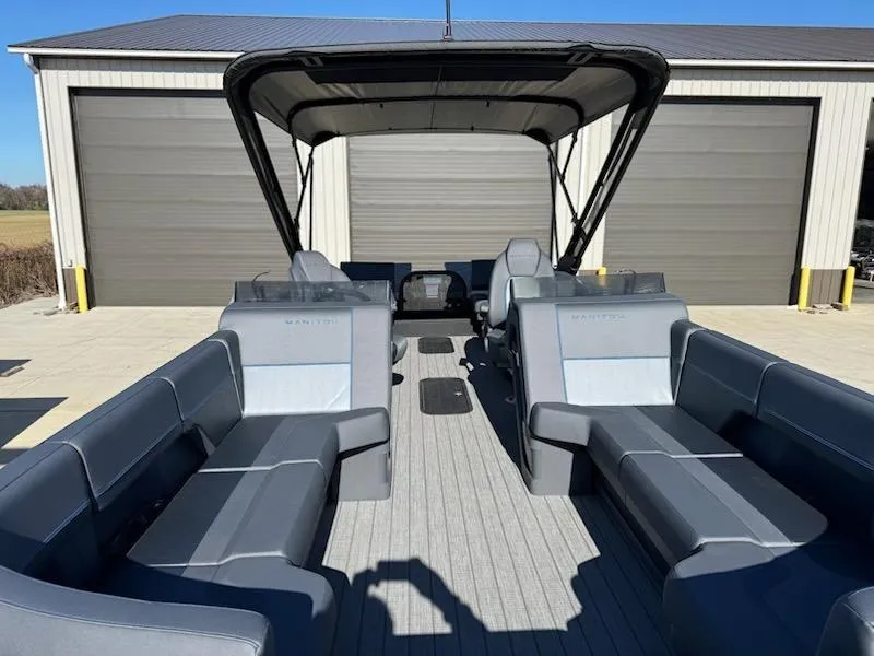 Slide: The Image of 2025 Manitou Navigator pontoon boat with spacious seating and canopy, parked near garage. - 4
