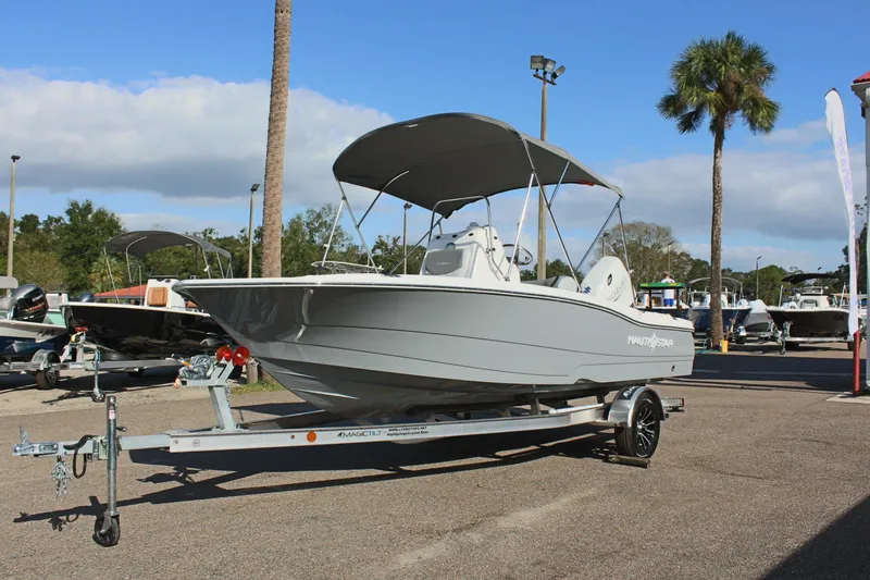 Slide: The Image of 2025 NauticStar 191 Hybrid boat on trailer, parked outdoors under a clear sky. - 2