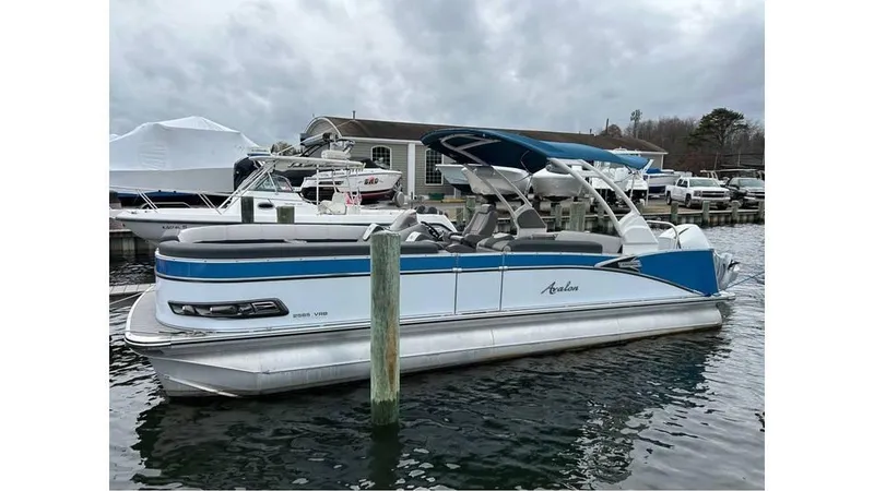 Slide: The Image of 2023 Avalon 2585 VRB pontoon boat docked in marina, overcast sky. - 2