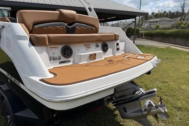 Slide: The Image of 2025 Four Winns HD3 boat with tan seating and swim platform, parked on grass. - 19