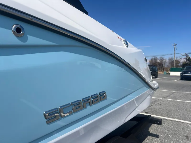 Slide: The Image of 2024 Scarab 255 ID boat, light blue and white exterior, parked outdoors under clear sky. - 23