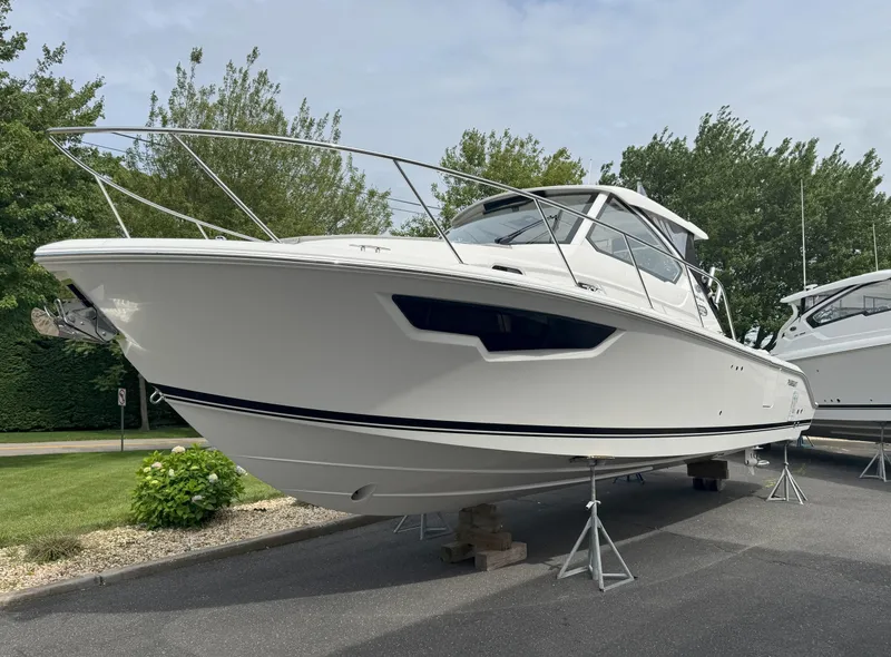 Slide: The Image of 2025 Pursuit OS 325 Offshore boat on display, elevated on stands, surrounded by greenery. - 2