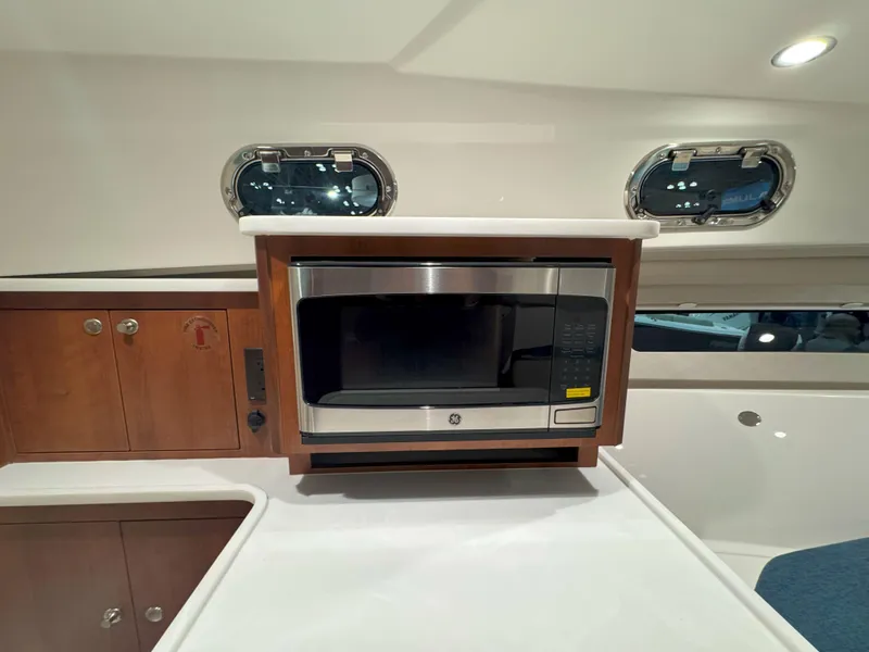 Slide: The Image of 2025 Pursuit OS 325 Offshore interior with microwave and wooden cabinetry. - 23