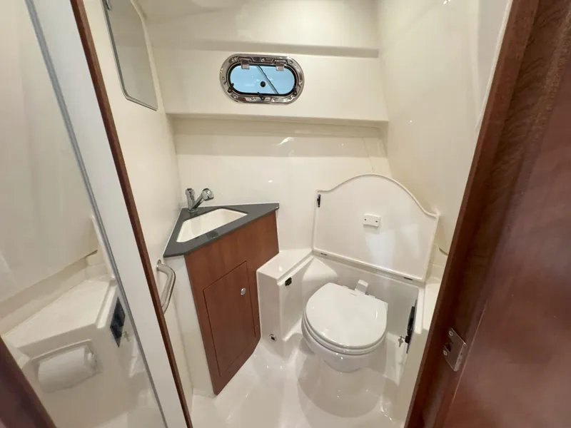 Slide: The Image of 2025 Pursuit OS 325 Offshore boat bathroom with sink, toilet, and porthole window. - 27