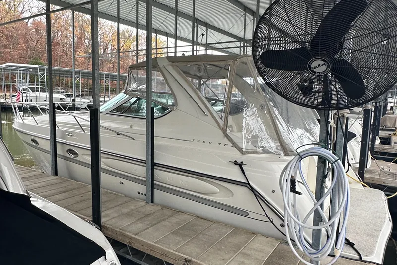 Slide: The Image of 1998 Maxum 3700 SCR boat docked under a covered marina with a large fan nearby. - 10