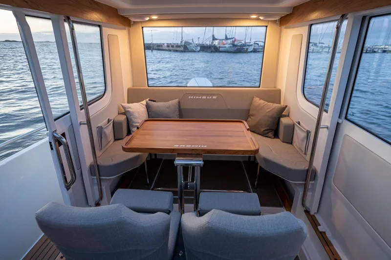 Slide: The Image of Interior of 2025 Nimbus C9 boat with cozy seating and wooden table, overlooking marina. - 4