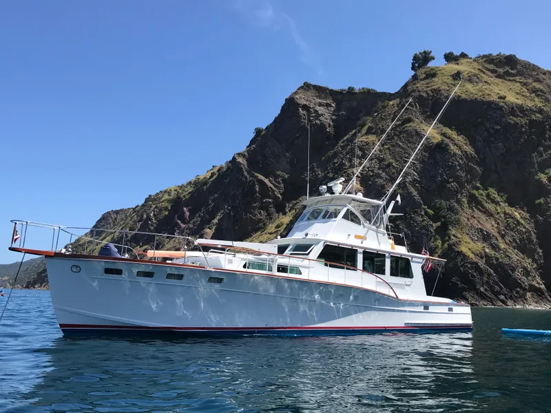 Slide: The Image of 1966 Huckins Sportsman yacht anchored near rocky coastline under clear blue sky. - 1