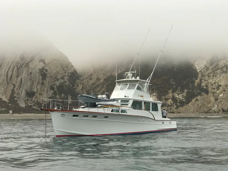 Slide: The Image of 1966 Huckins Sportsman yacht on misty water near rocky cliffs. - 6