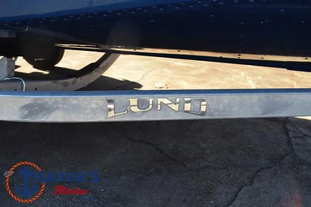 Slide: The Image of 2024 Lund 1650 Angler Tiller boat trailer with logo, displayed on concrete surface. - 6