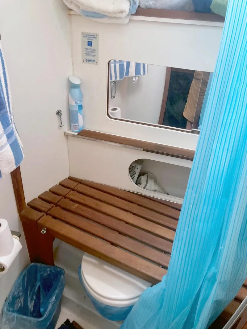 Slide: The Image of 1983 Hunter 34 sailboat bathroom with wooden bench, mirror, and blue shower curtain. - 16