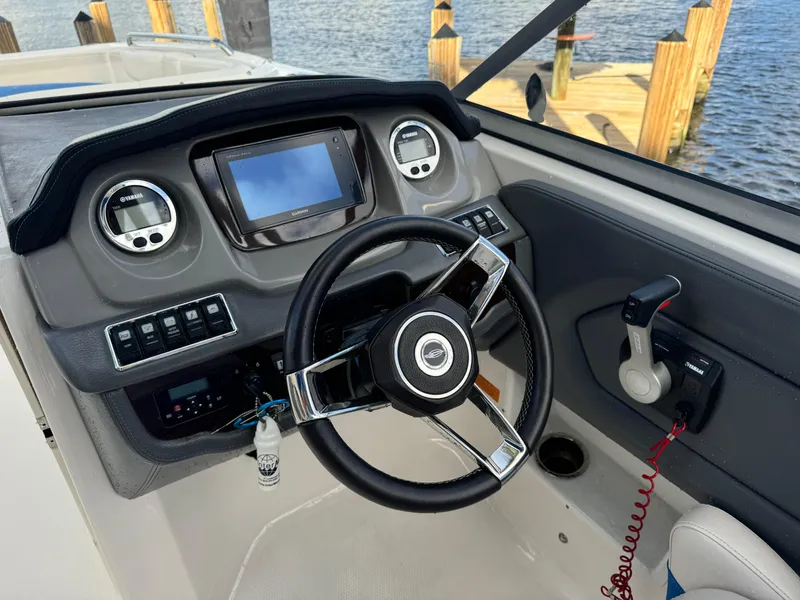 Slide: The Image of 2017 Chaparral 250 Suncoast boat dashboard with steering wheel and controls by the water. - 11