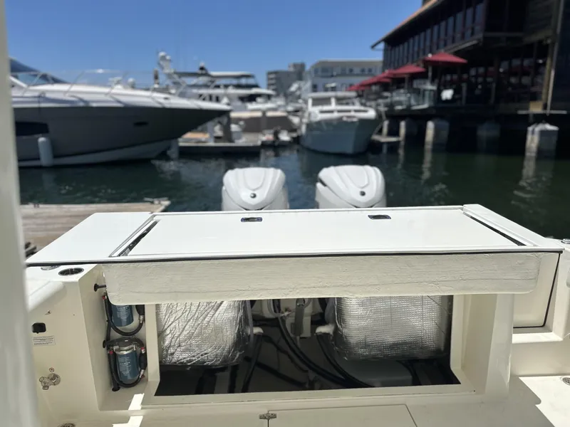 Slide: The Image of 2024 Cobia 320 Center Console at marina, showcasing engine compartment and docked boats. - 4