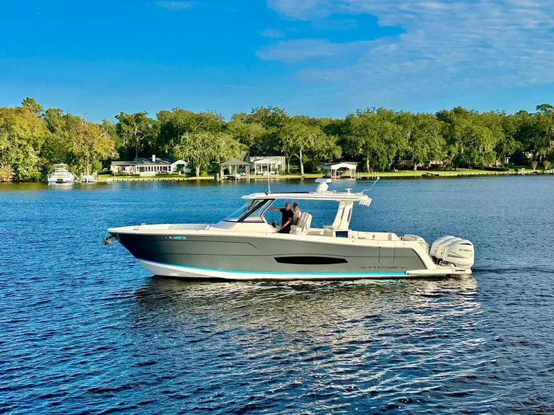 Slide: The Image of 2021 Regal 38 SAV boat cruising on a scenic lake with lush greenery. - 1