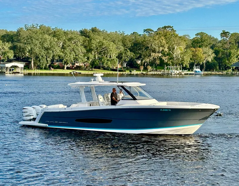 Slide: The Image of 2021 Regal 38 SAV boat cruising on a scenic lake with lush greenery. - 2
