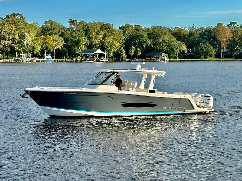 Slide: The Image of 2021 Regal 38 SAV boat cruising on a serene lake with lush green shoreline. - 4