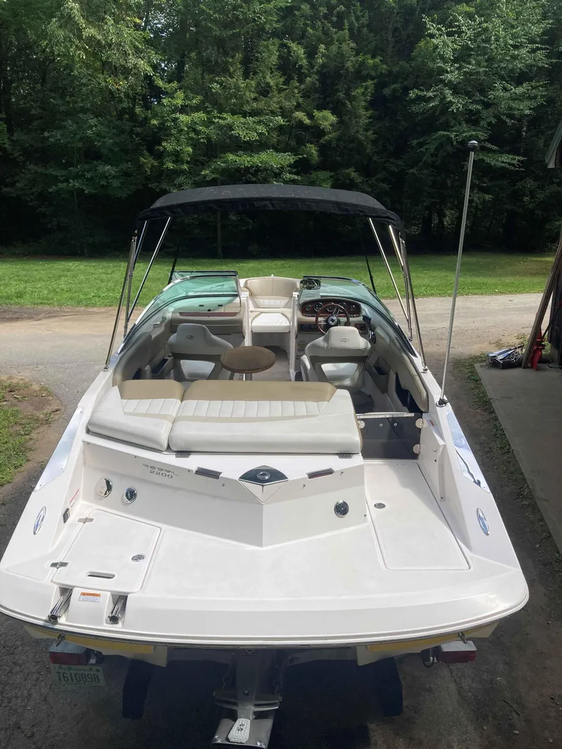 Slide: The Image of 2011 Regal 2200 boat with canopy, parked on a driveway, surrounded by trees. - 3