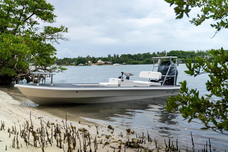 Slide: The Image of 2025 BlueZones Boatworks 16' Flats boat docked by a serene shoreline. - 24