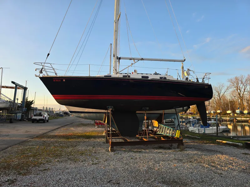 Slide: The Image of 1988 Tartan 31 sailboat on dry dock, black hull with red stripe, marina background. - 2